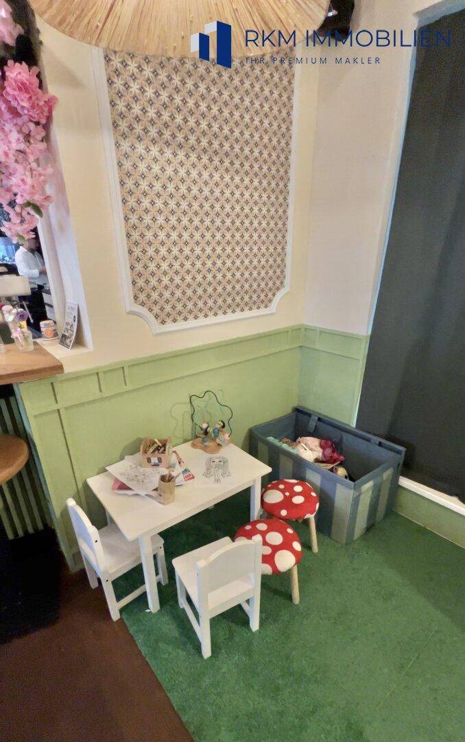 Kleiner Spielbereich für Kinder mit Tisch, Stühlen und Pilzhockern in einem Café.