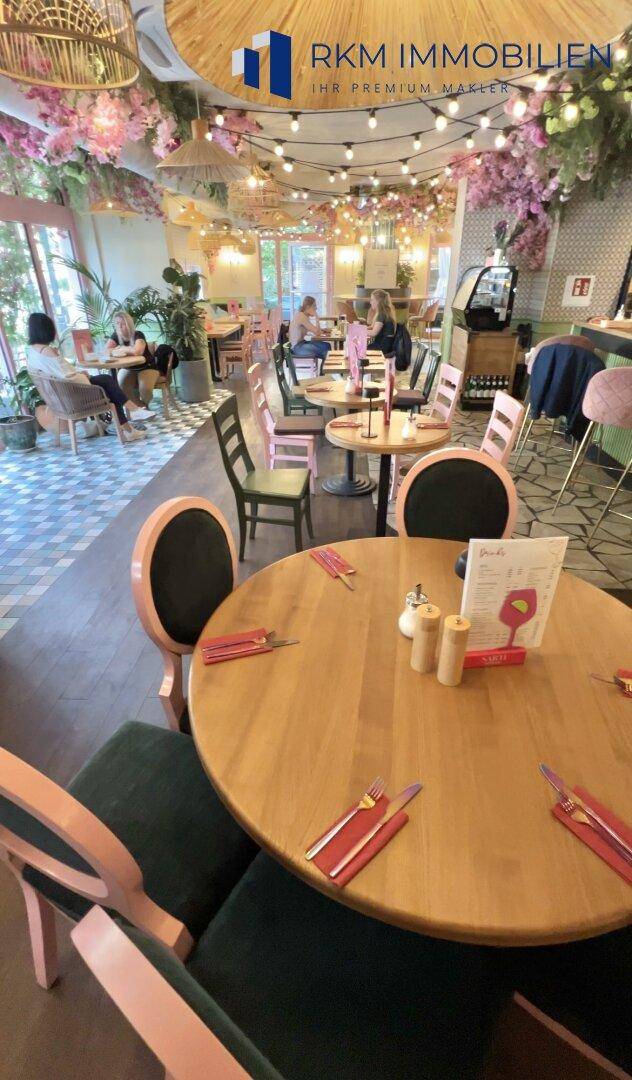 Geräumiger Restaurantbereich mit verschiedenen Tischen und Stühlen, umgeben von floraler Dekoration.