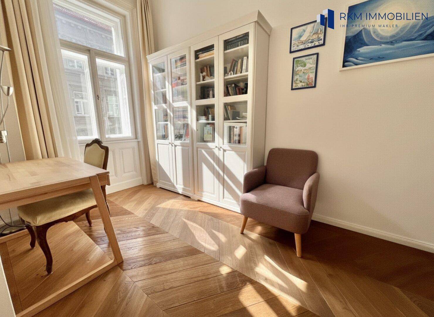 Freundlicher Raum mit Bücherregal, Schreibtisch und Fischgrätparkett, ideal als Arbeitszimmer nutzbar.