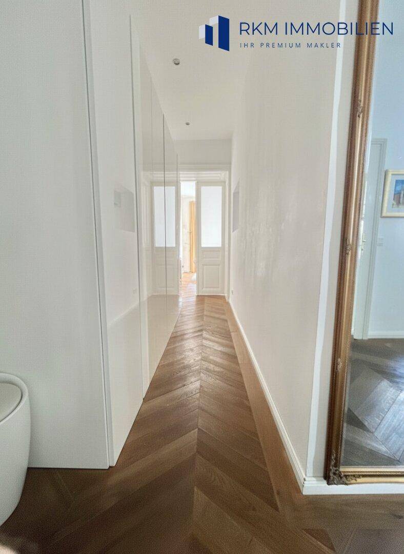 Langer, heller Flur mit elegantem Fischgrätparkett und einem großen Wandspiegel.