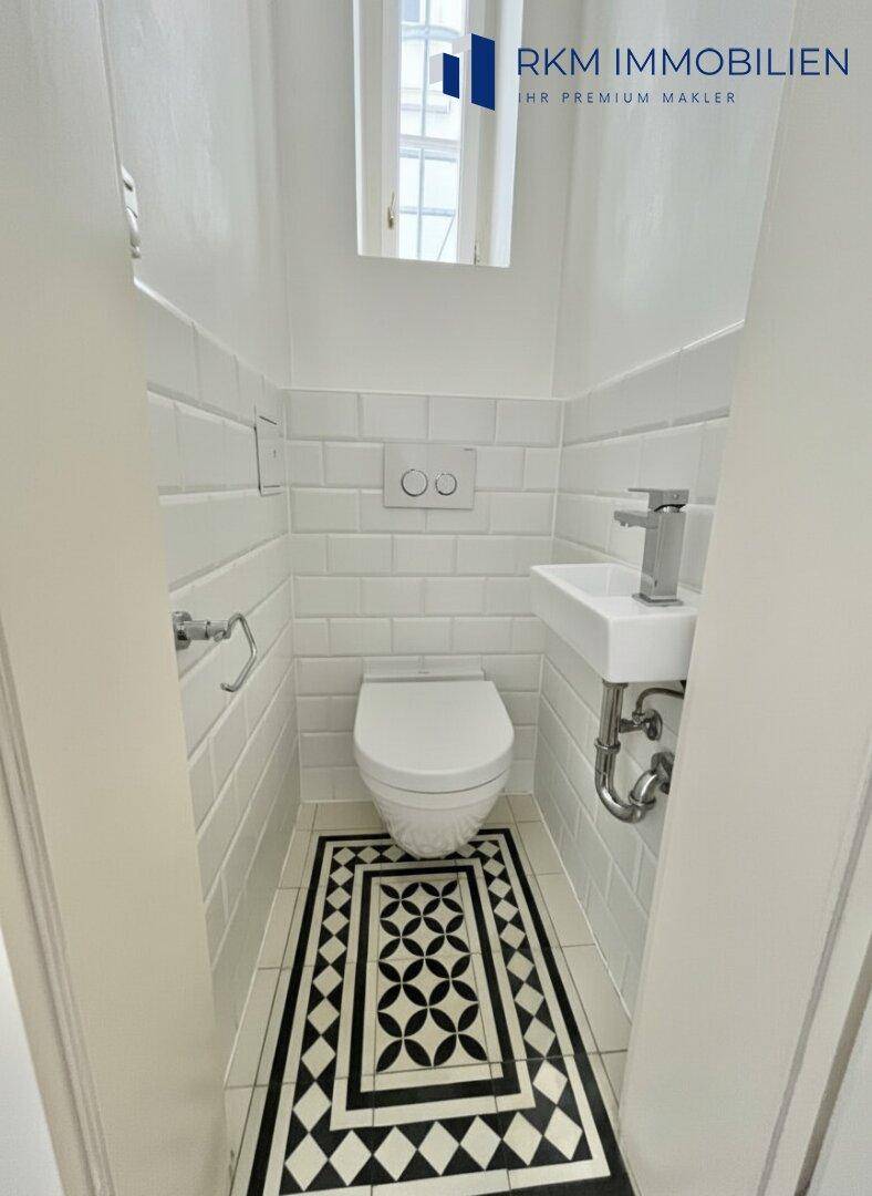 Kompaktes Gäste-WC mit wandhängender Toilette, kleinem Waschbecken und dekorativen Bodenfliesen.