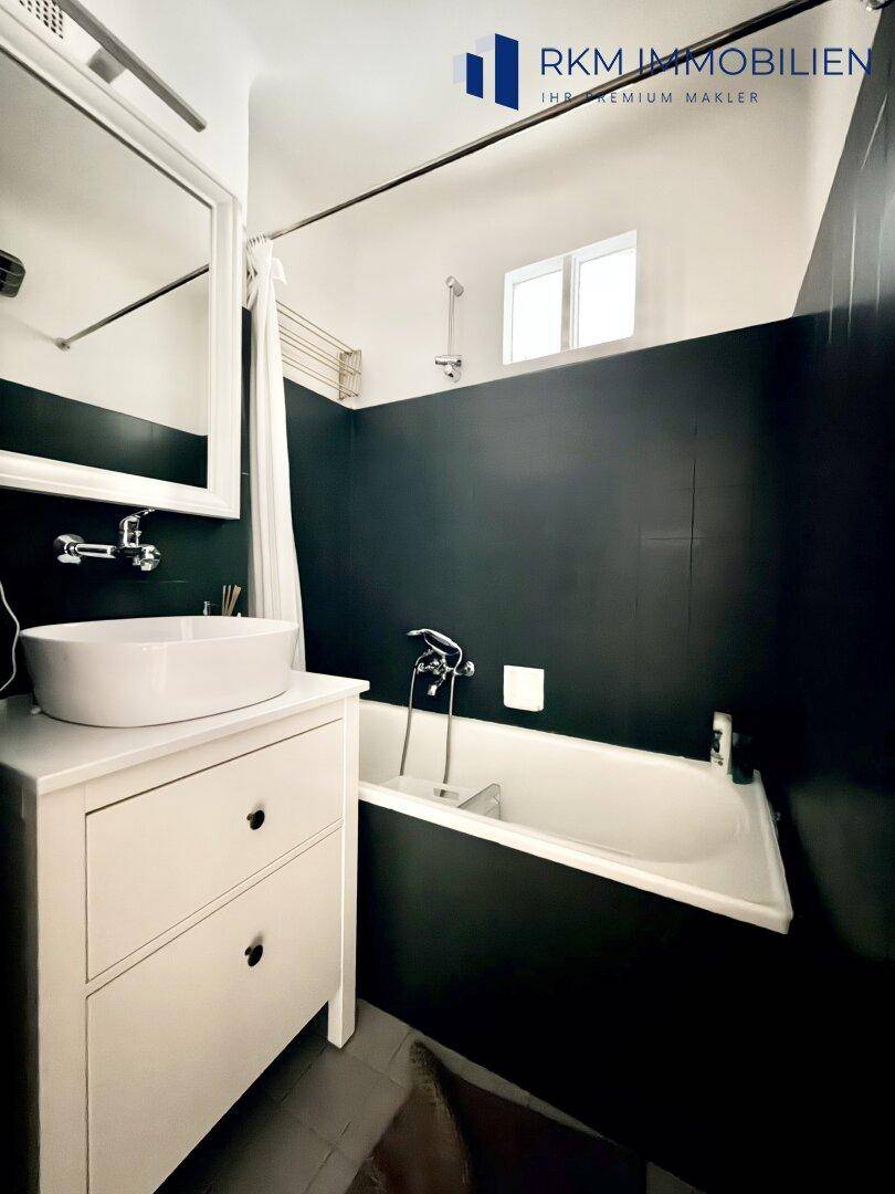Modernes Badezimmer mit Badewanne, Einzelwaschbecken und dunklen Fliesen an den Wänden.