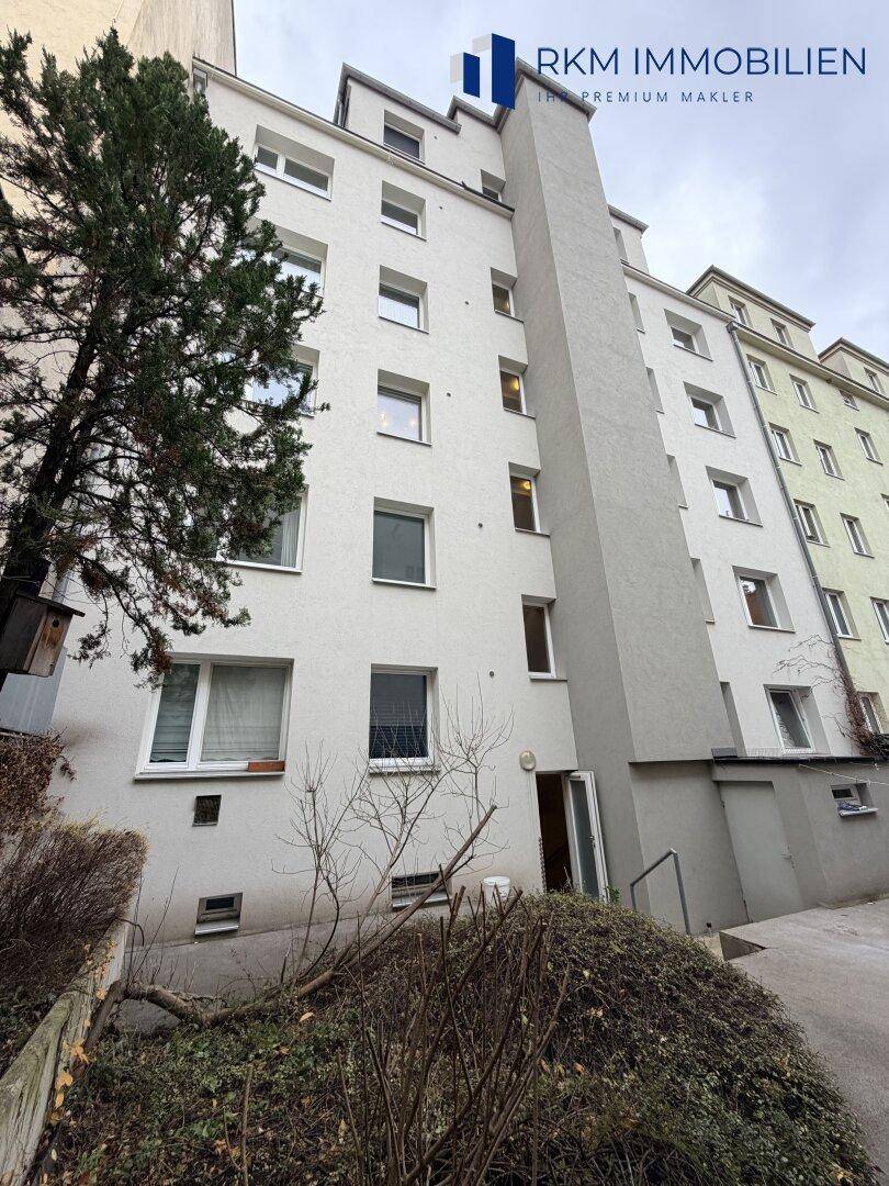 Mehrstöckiges Wohngebäude mit weißer Fassade und mehreren Fenstern, umgeben von Vegetation.