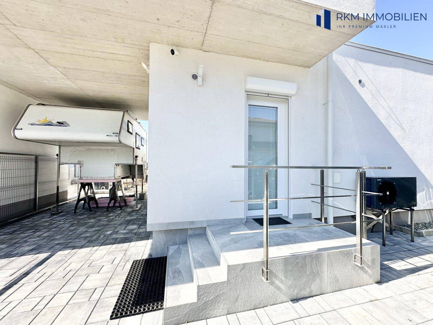 Eingangsbereich des Hauses mit Treppe und Geländer, daneben ein Carport mit Wohnmobil.