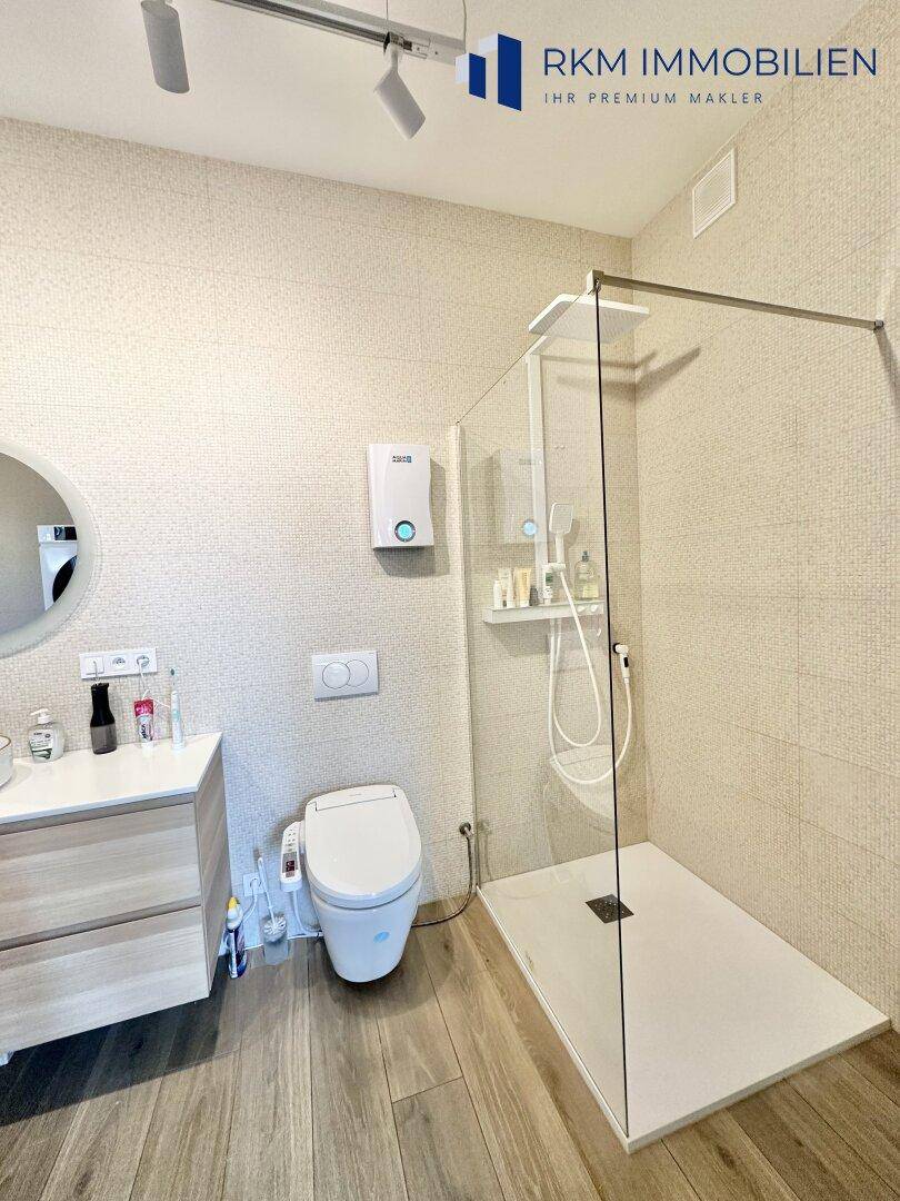 Modernes Badezimmer mit ebenerdiger Dusche, wandhängendem WC und stilvollem Einzelwaschbecken.