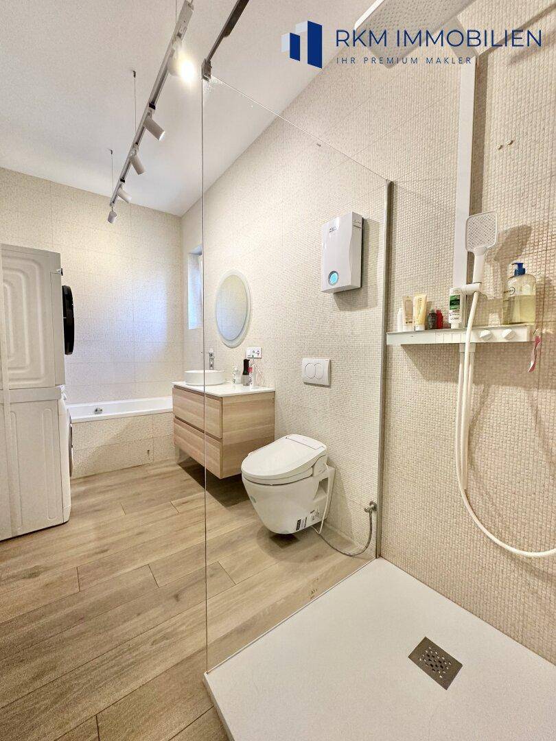 Geräumiges Badezimmer mit begehbarer Dusche, Badewanne und integrierter Waschmaschine.