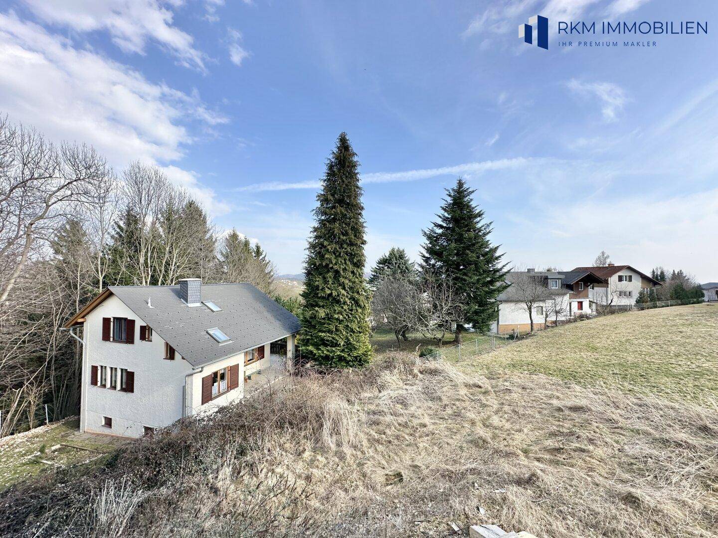 Weitläufiger Blick über die grüne Landschaft mit einem benachbarten Haus und hohen Bäumen.