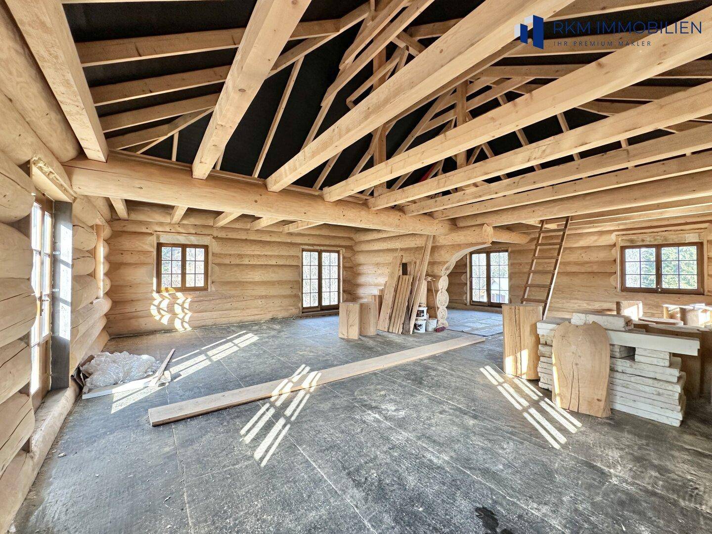 Geräumiger, unfertiger Innenraum mit Holzstammwänden, offener Dachkonstruktion und hellen Fenstern.