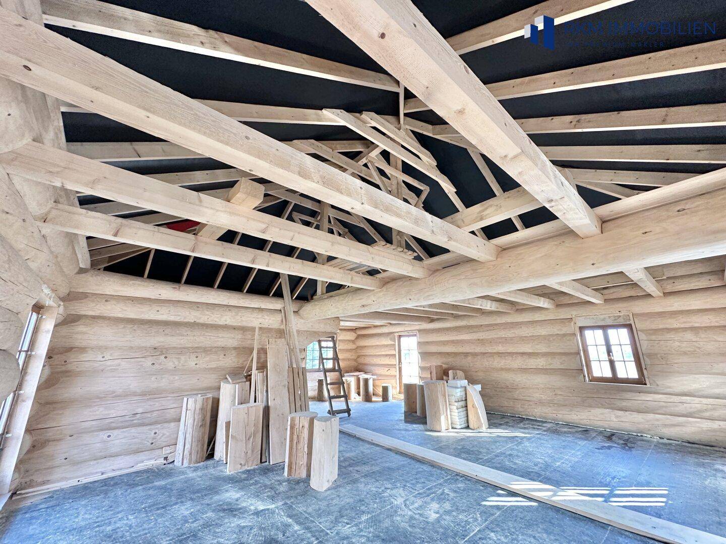 Weitwinkelaufnahme des unfertigen Innenraums mit dominierenden Holzbalken und Blockwänden.