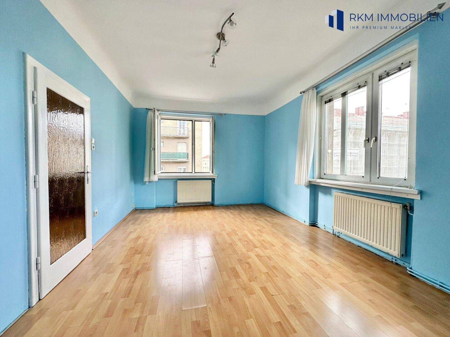 Schlafzimmer mit blau gestrichenen Wänden, Laminatboden und zwei Fenstern.