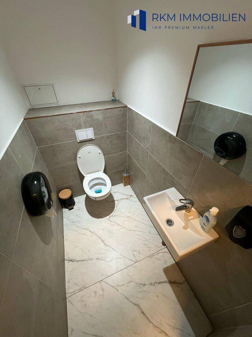 Moderne Toilette mit Wand-WC, kleinem Waschbecken und großformatigen Fliesen an Wänden und Boden.