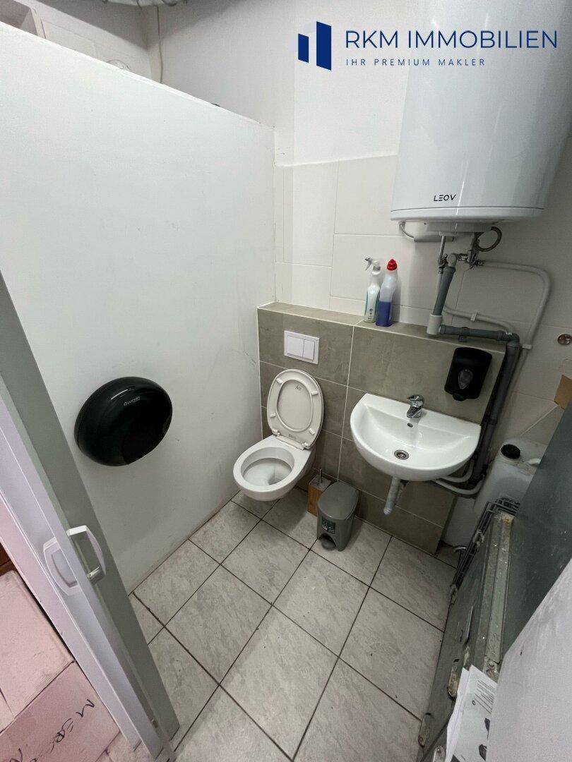 Einfache Personaltoilette mit WC, Waschbecken und Boiler, funktional eingerichtet, mit Fliesenboden.