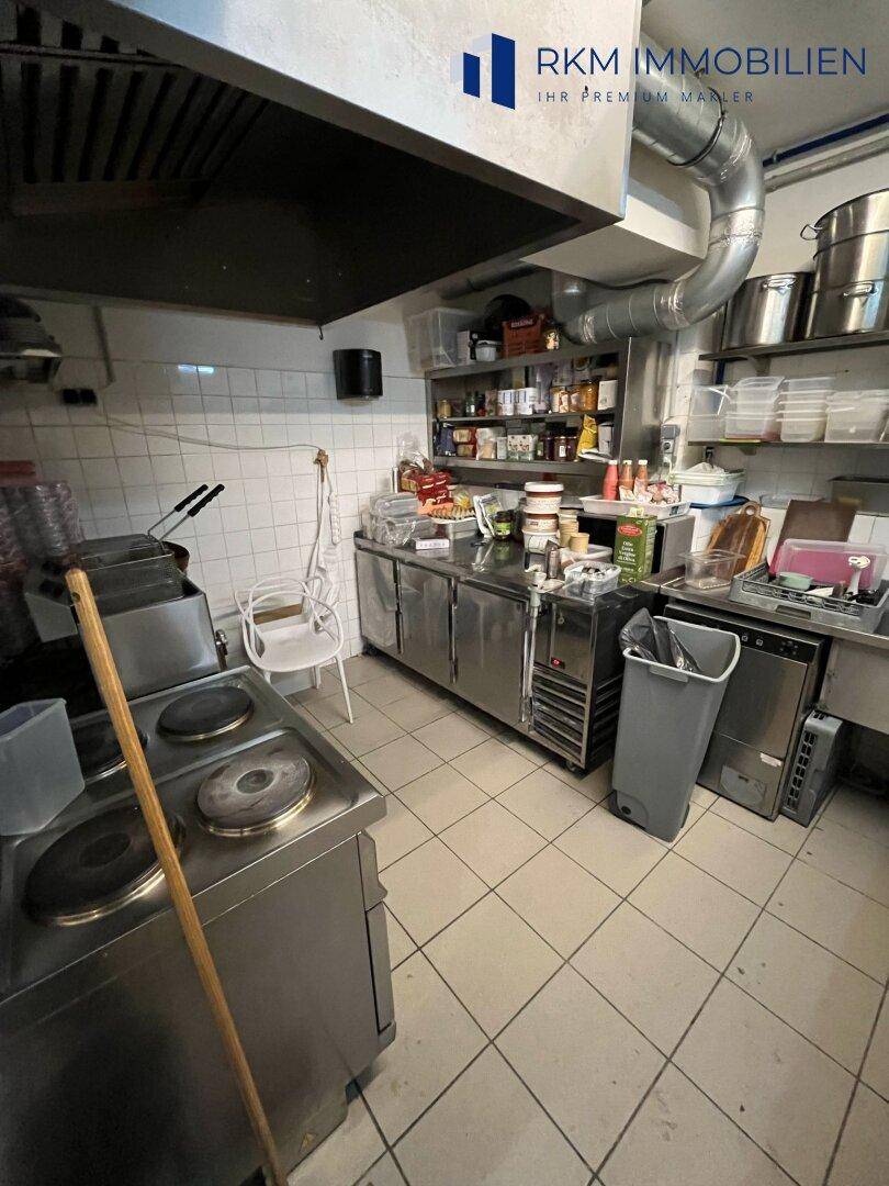 Gewerbliche Küche mit Edelstahlgeräten, Fliesenwänden und einer großen Dunstabzugshaube, funktional eingerichtet.