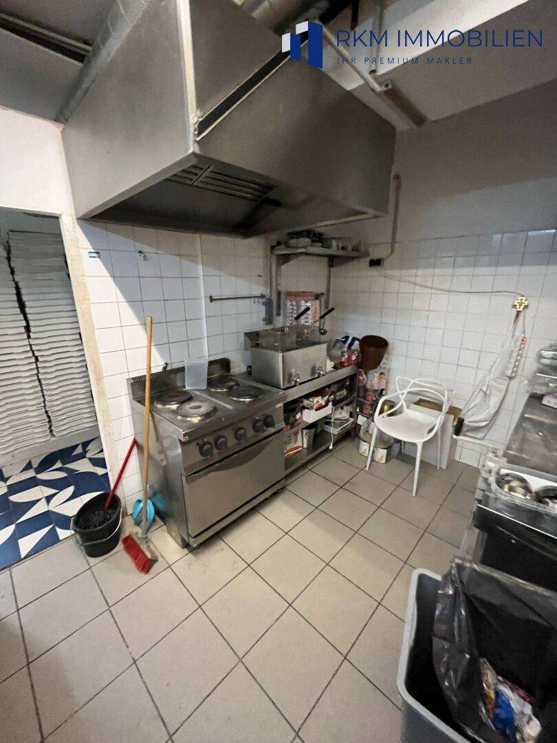 Funktionale Küche mit professionellem Herd, Fritteuse und Edelstahlflächen, bereit für den Betrieb, mit Fliesenboden.