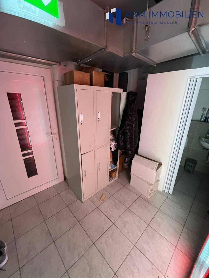Personalbereich mit Spinden und Zugang zu einer Toilette, funktional eingerichtet, mit Fliesenboden.