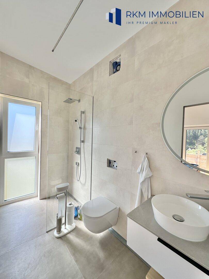 Modernes Badezimmer mit begehbarer Dusche, Wand-WC und großformatigen Fliesen.