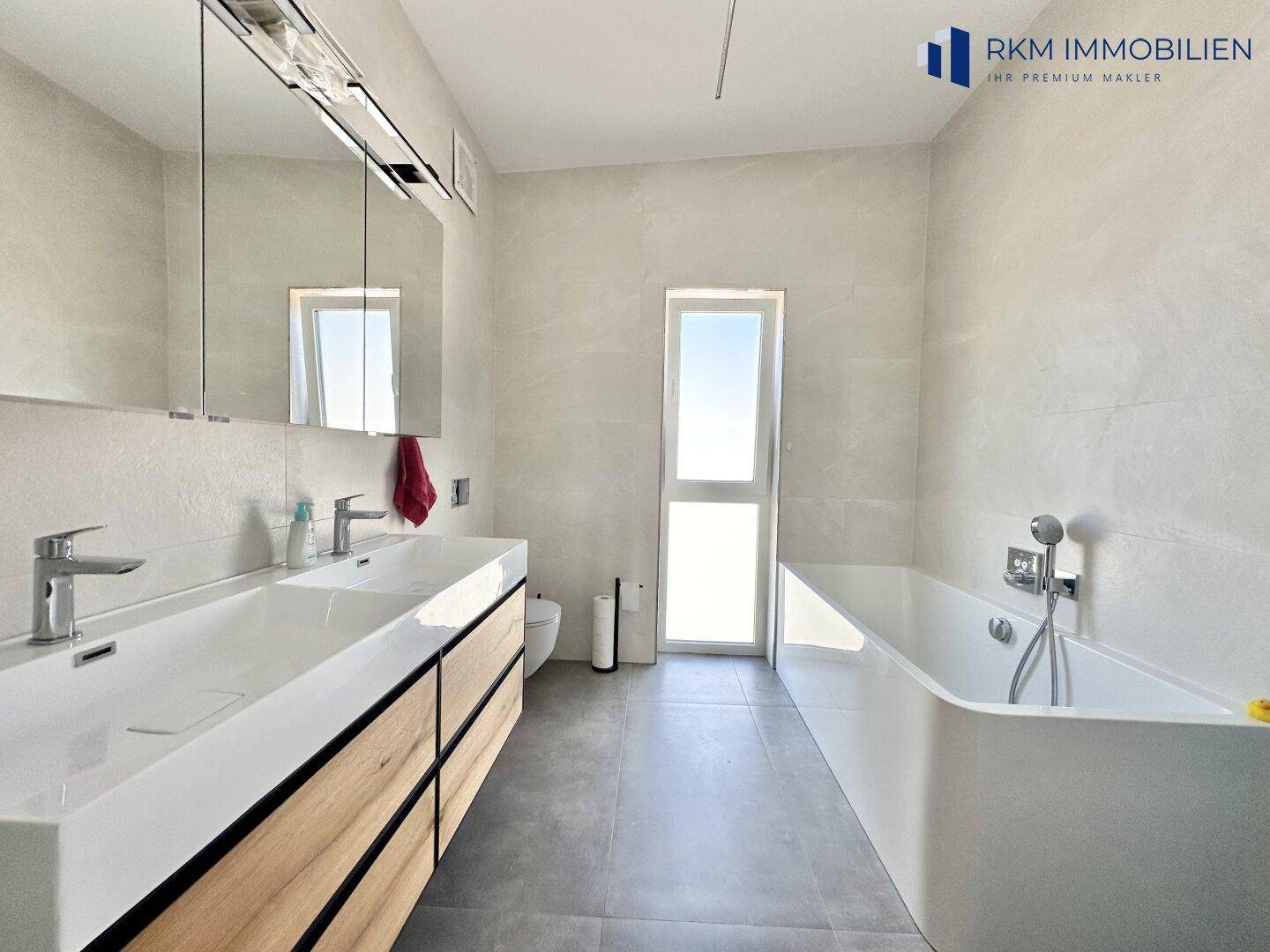 Geräumiges Badezimmer mit Doppelwaschbecken, Badewanne und großem Fenster.