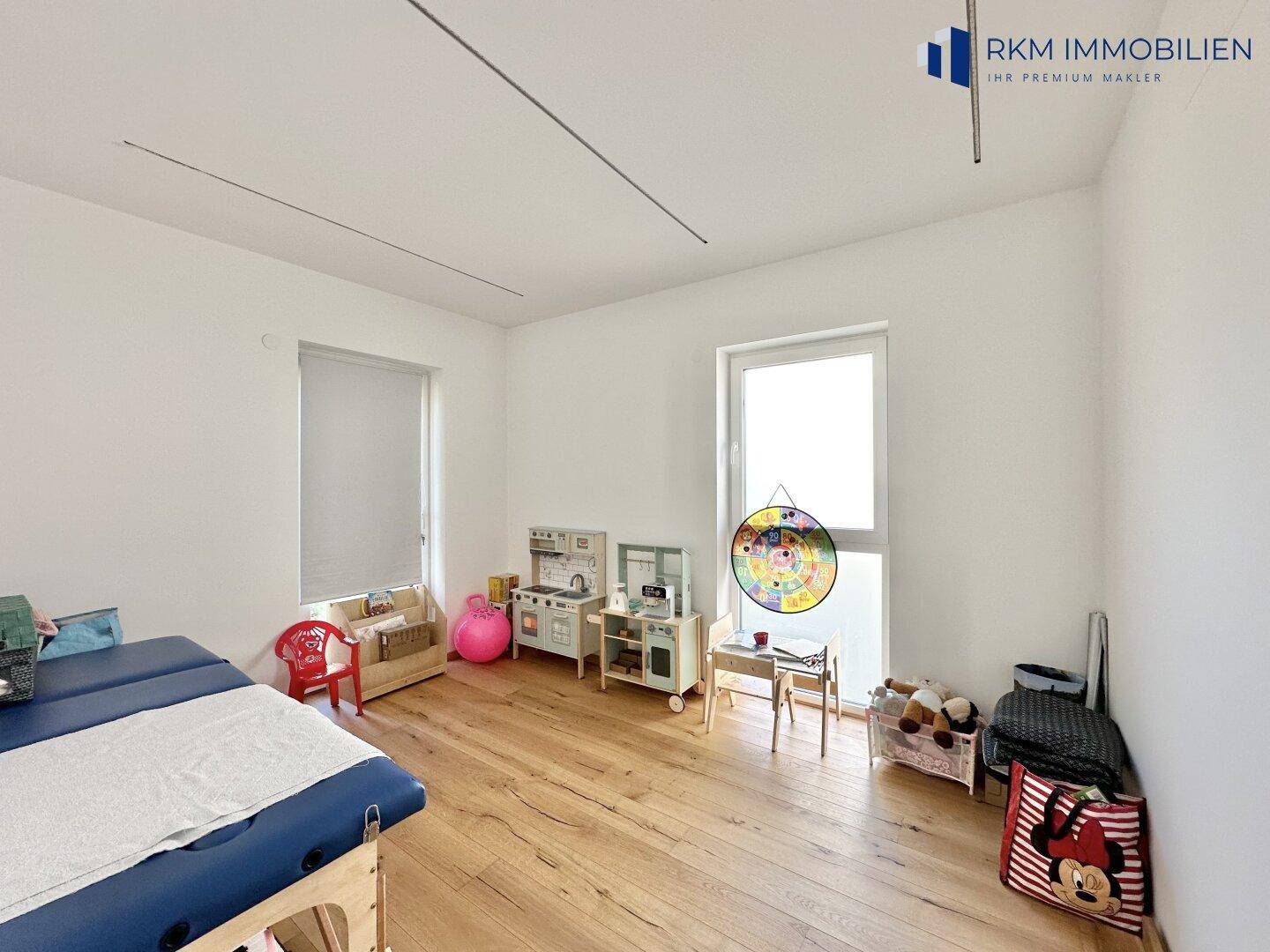 Helles Kinderzimmer mit Holzboden, Spielzeug und großem Fenster.