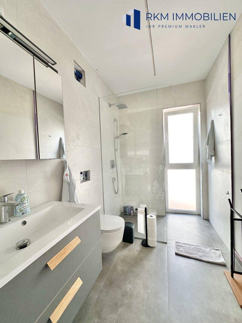 Modernes Badezimmer mit begehbarer Dusche, Einzelwaschbecken und hellen Fliesen.