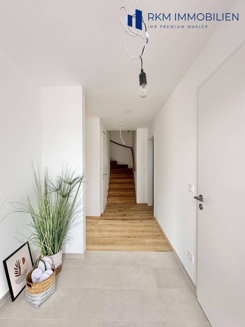 Heller Flur mit modernen Fliesen und Holztreppe, die in das obere Stockwerk führt.