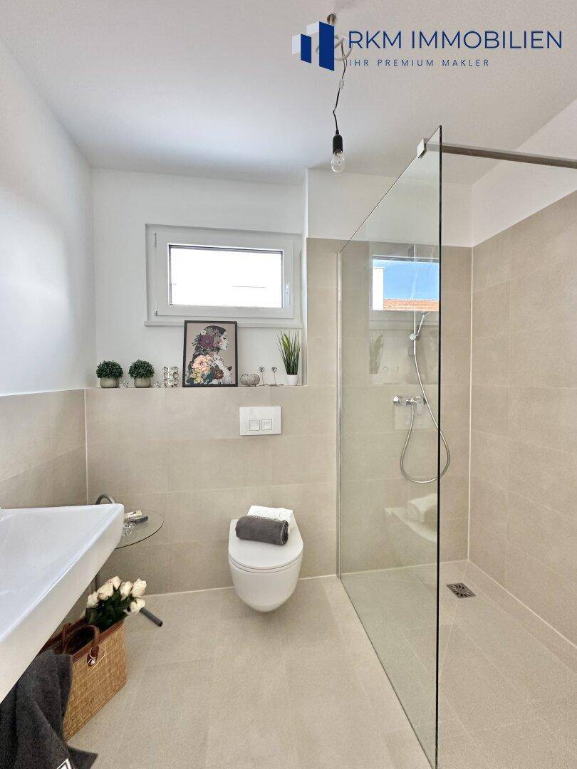 Modernes Badezimmer mit ebenerdiger Dusche, Wand-WC und Fenster für natürliche Belüftung.