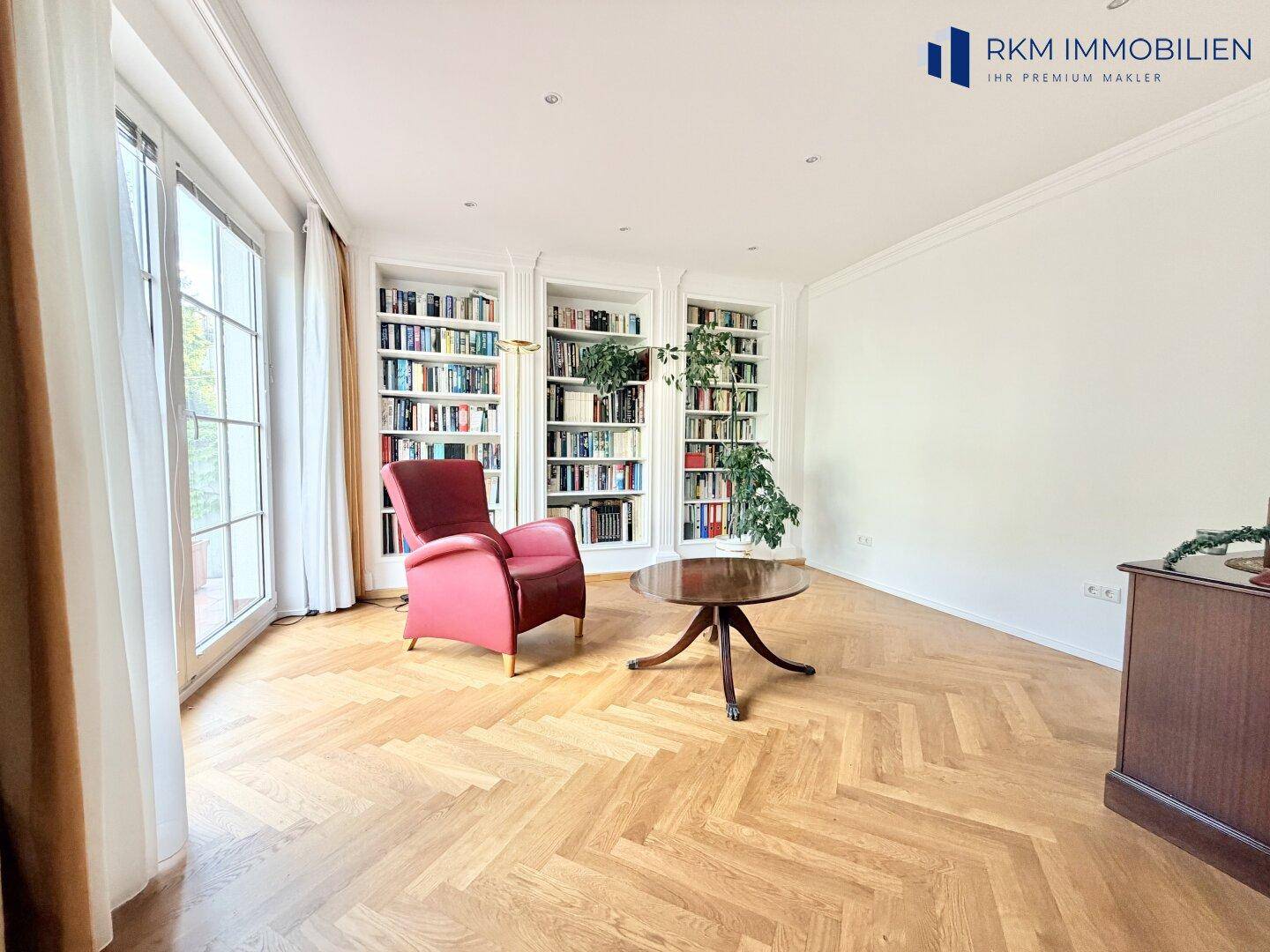 Gemütlicher Bereich mit eingebauten Bücherregalen, einem roten Sessel und Zugang zum Außenbereich.