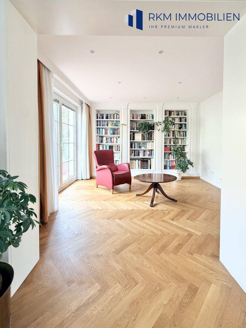 Heller Wohnbereich mit Fischgrätparkett, raumhohen Bücherregalen und großen Fenstern zum Garten.
