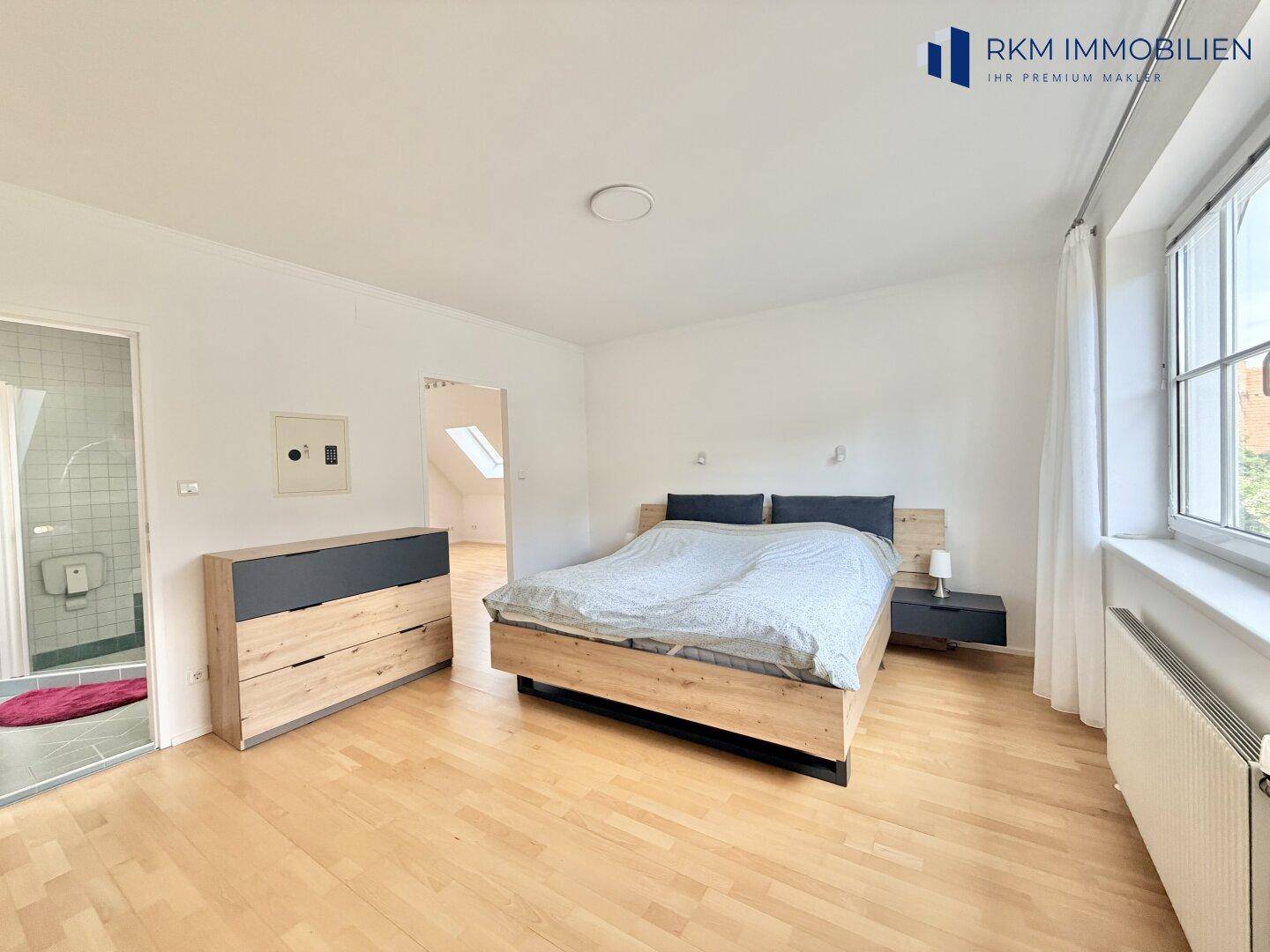 Geräumiges Schlafzimmer mit Holzboden, Doppelbett und Zugang zu einem angrenzenden Badezimmer.