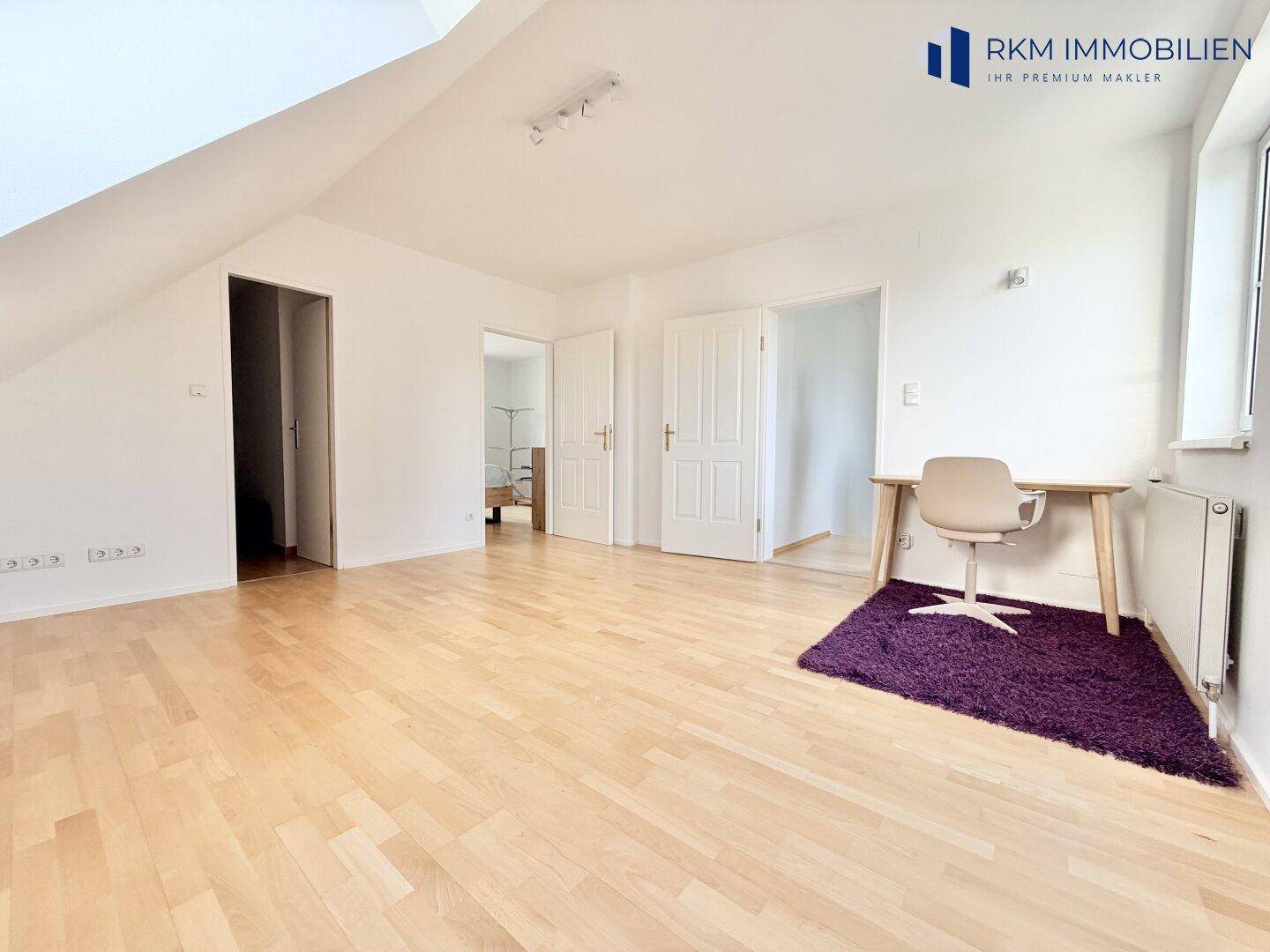 Helles Zimmer im Dachgeschoss mit Holzboden, Schreibtisch und mehreren Türen zu anderen Räumen.