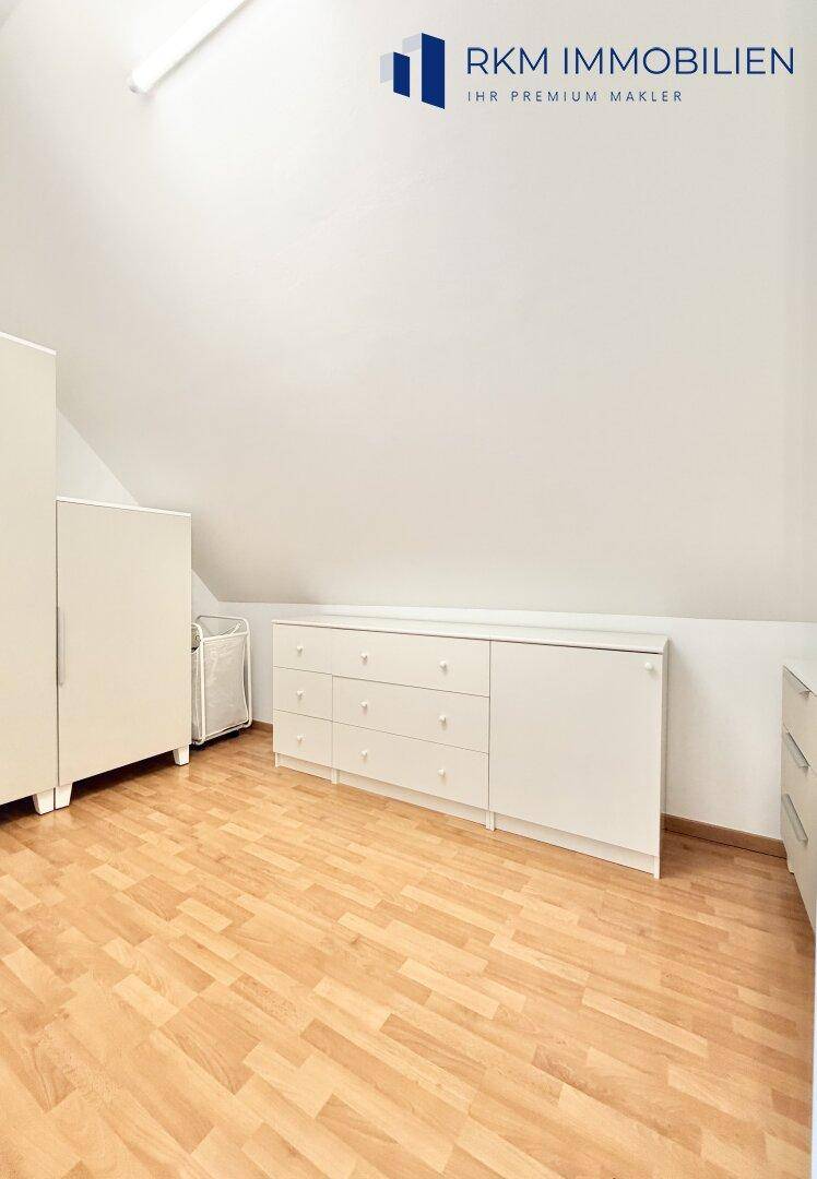 Dachzimmer mit Holzboden und weißen Möbeln, bietet zusätzlichen Wohn- oder Stauraum.