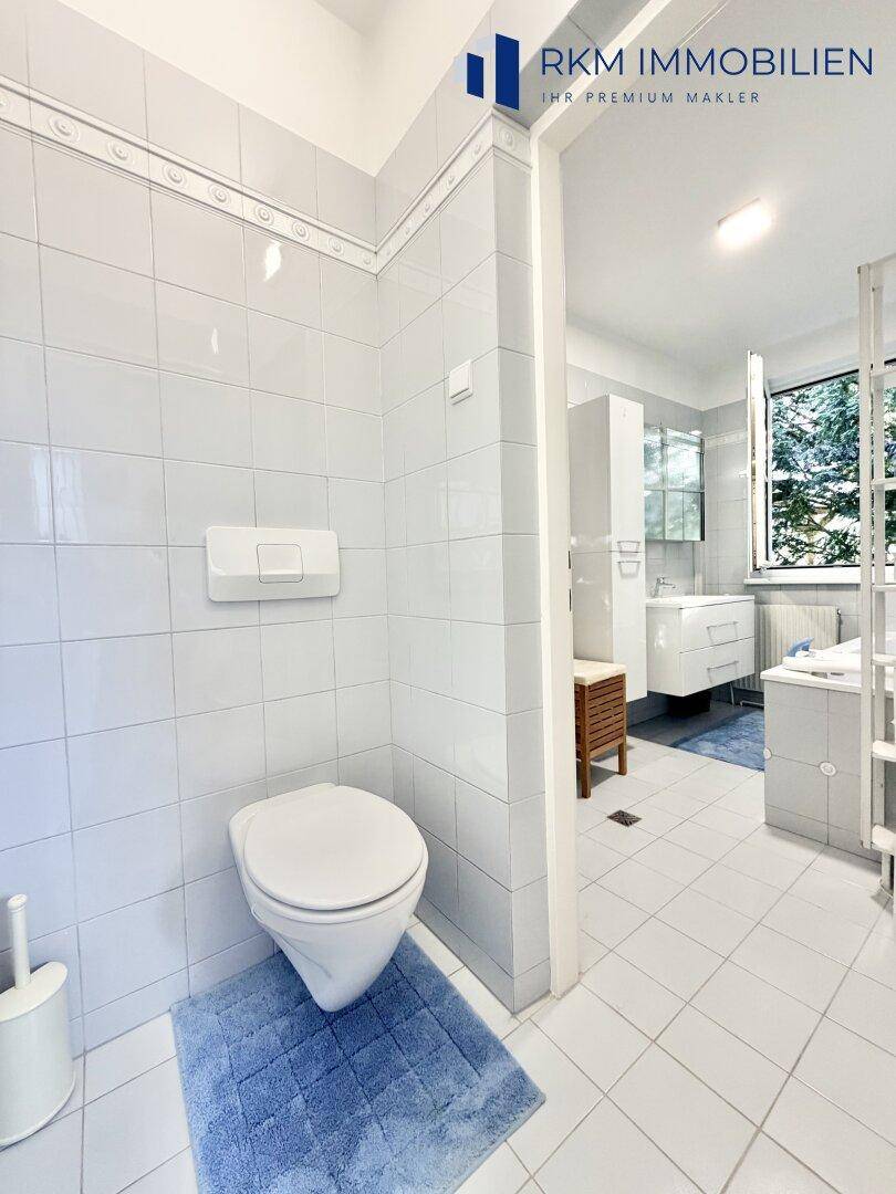 Separates WC mit weißen Fliesen und wandmontierter Toilette, neben dem Badezimmer gelegen.