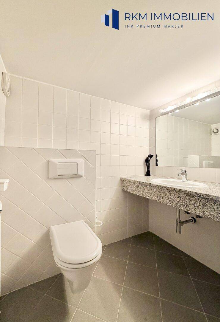 Modernes Gäste-WC mit Granitwaschtisch, wandmontierter Toilette und grauen Bodenfliesen.