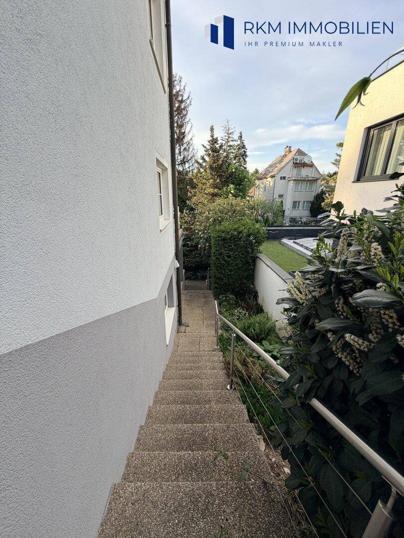 Ein langer Außentreppenweg führt durch üppiges Grün und Bäume zu weiteren Häusern.