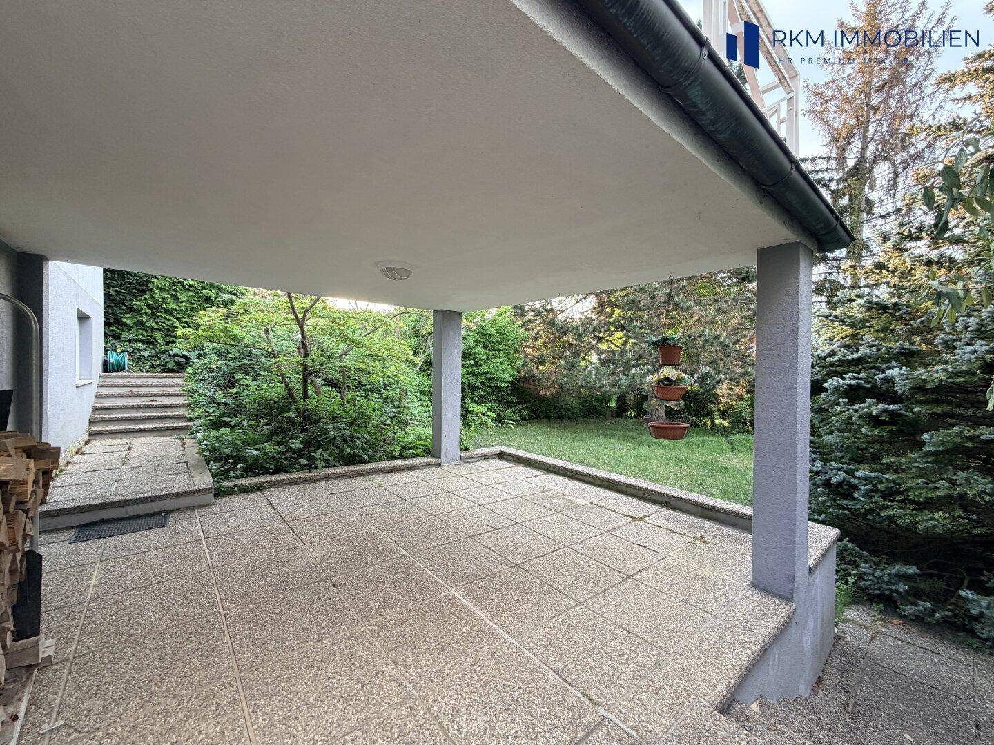 Eine überdachte Terrasse mit Fliesenboden bietet einen direkten Zugang zum grünen Gartenbereich.