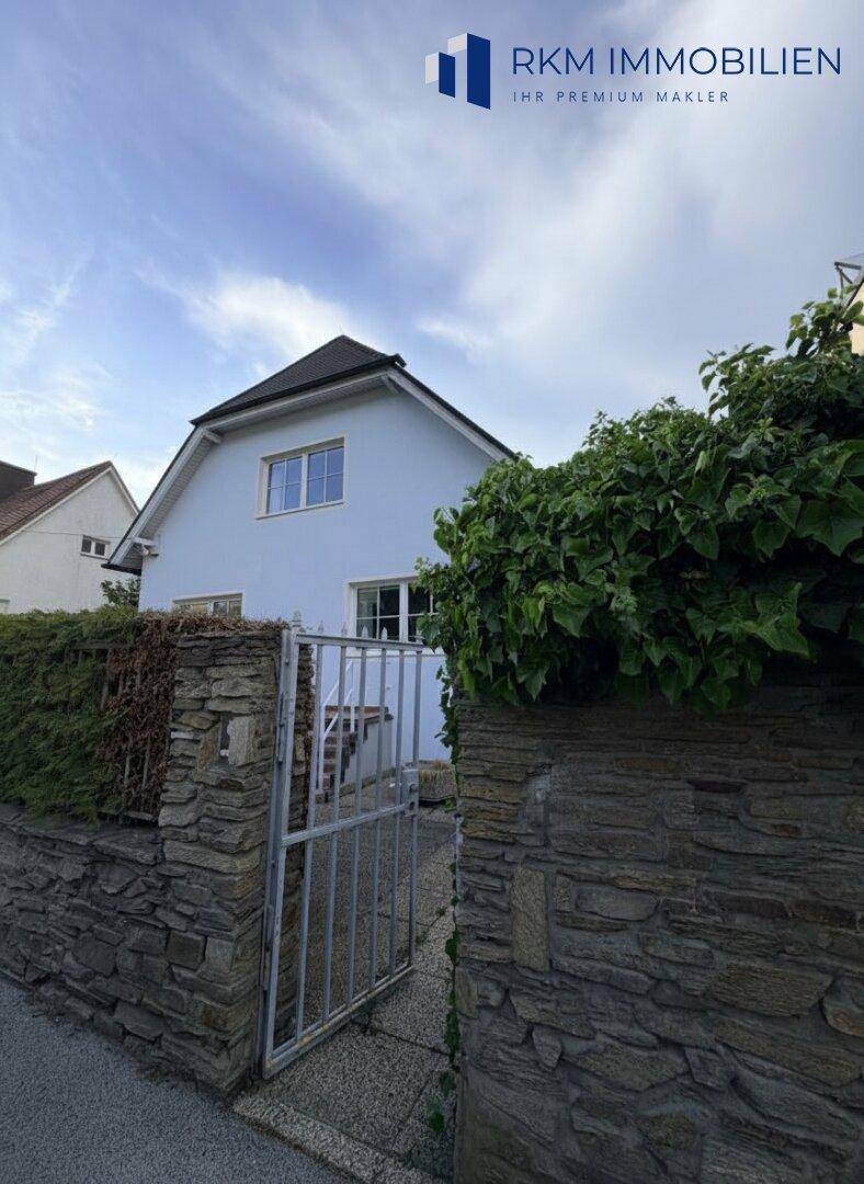 Eingangsbereich des Hauses mit Steinmauer und einem grünen Zaun, der Privatsphäre bietet.