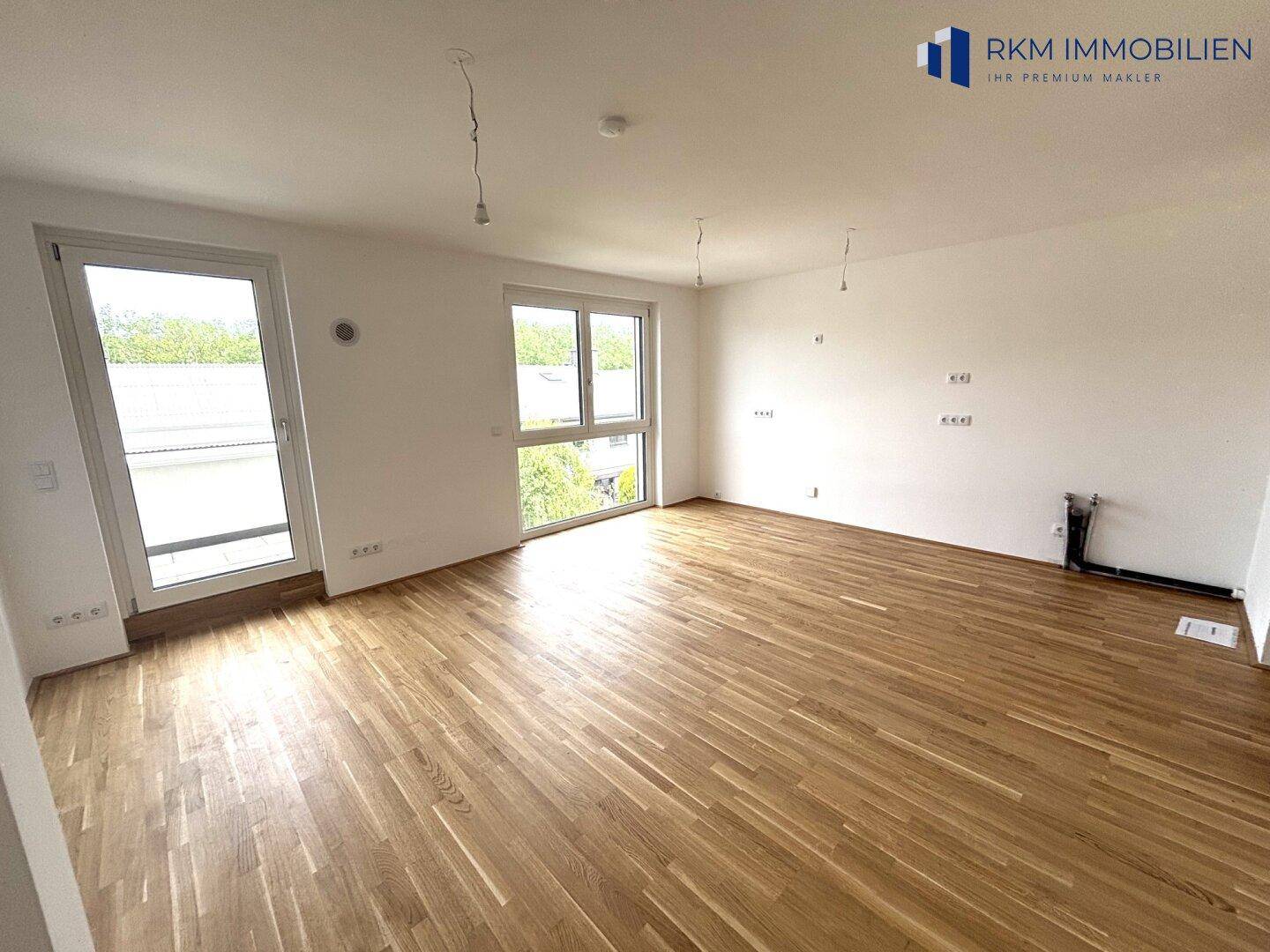Geräumiges, leeres Wohnzimmer mit Parkettboden und großen Fenstern, bietet viel Gestaltungspotenzial.
