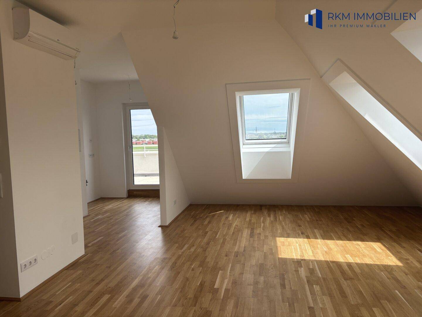 Dachgeschosszimmer mit Parkettboden, Dachfenstern und Zugang zu einer Terrasse, sehr hell.