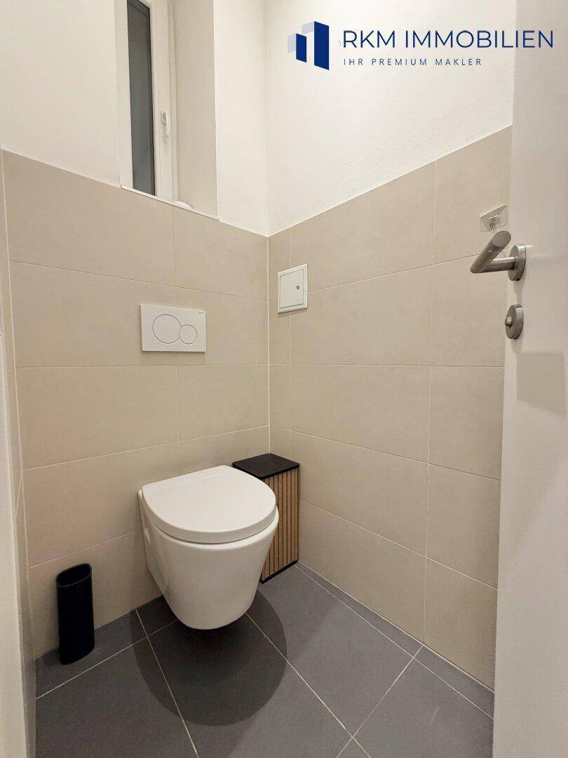 Separates WC mit wandhängender Toilette und beigefarbenen Wandfliesen, funktional und sauber.