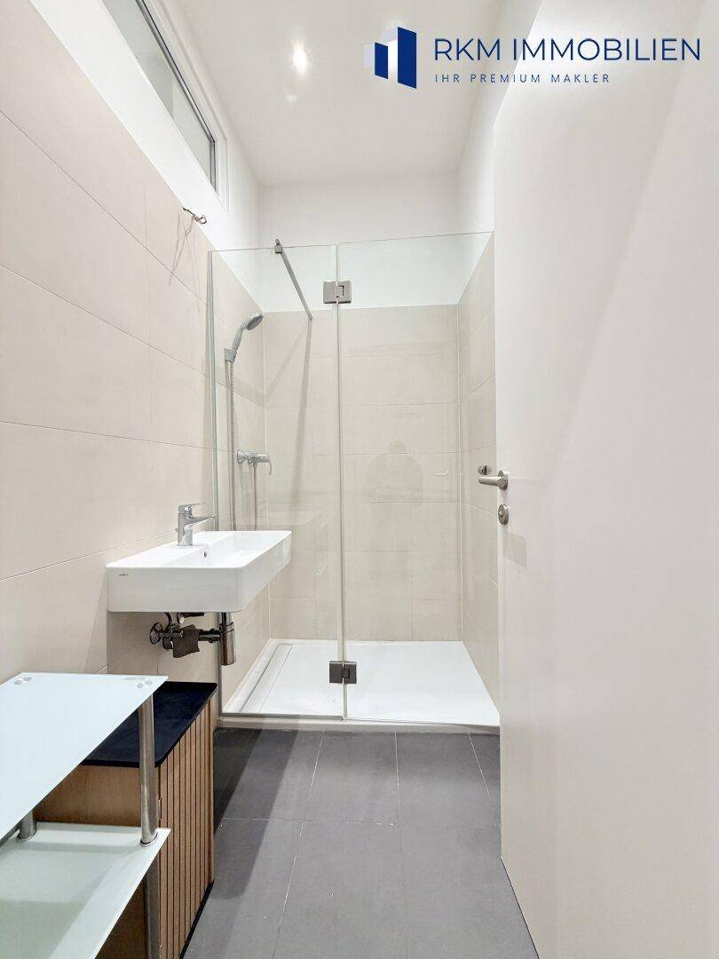Modernes Badezimmer mit begehbarer Dusche, Waschbecken und hellen Fliesen, gut beleuchtet.