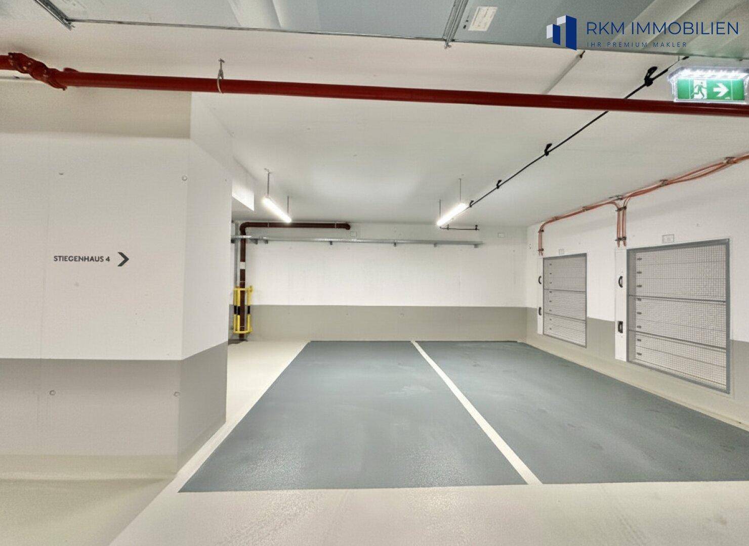 Saubere Tiefgarage mit markierten Stellplätzen, roten Leitungen und separaten Lagerabteilen.