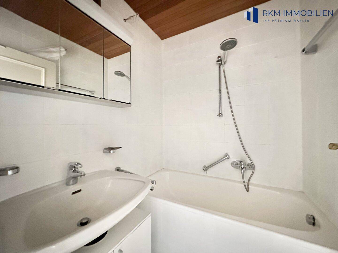 Helles Badezimmer mit Badewanne, Dusche, Einzelwaschbecken und Spiegelschrank, komplett gefliest.