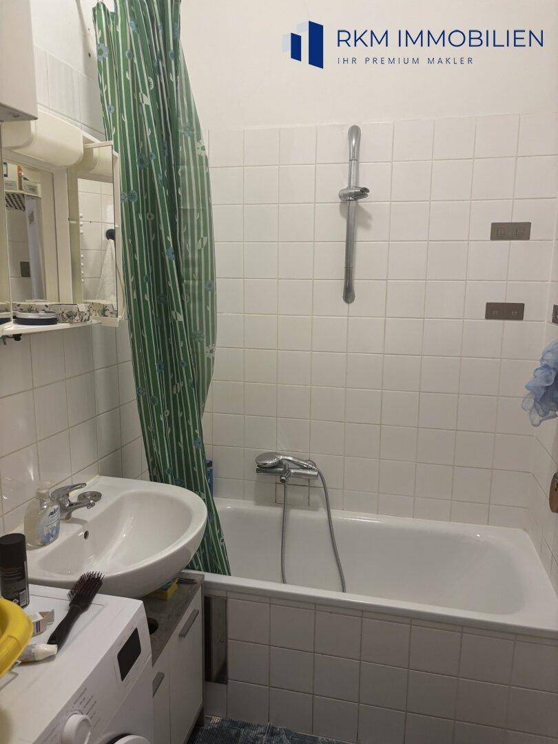 Badezimmer mit Badewanne, Waschbecken und weißen Fliesen, ausgestattet mit Duschvorhang und Spiegel.