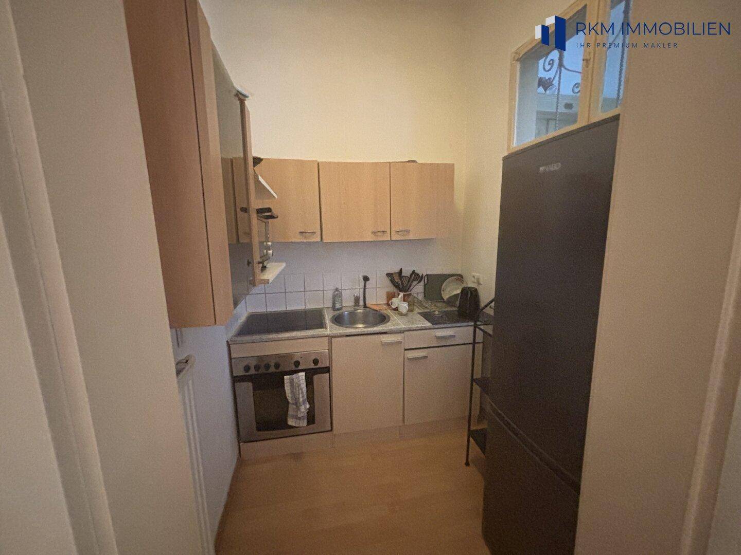 Kleine Einbauküche mit Holzschränken, Herd, Spüle und Kühlschrank, praktisch und funktional.