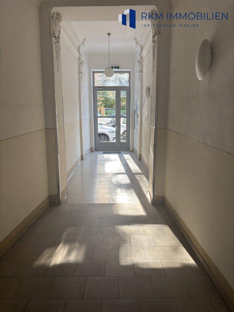 Heller Eingangsbereich mit Fliesenboden, Stuckverzierungen und Blick zur Straße, typisch Altbau.