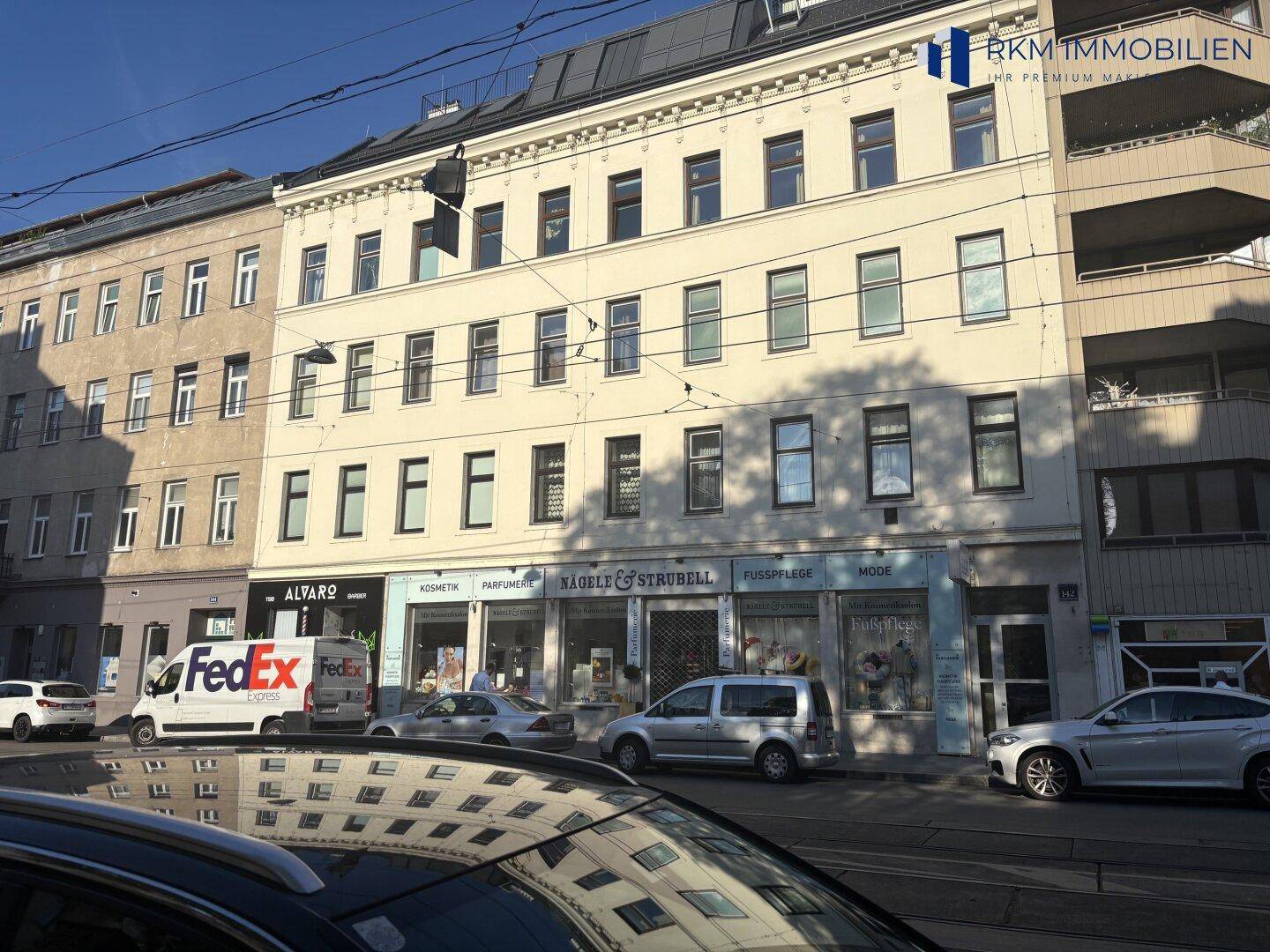 Mehrstöckiges Altbau-Wohn- und Geschäftshaus an einer belebten Straße mit Geschäften im Erdgeschoss.
