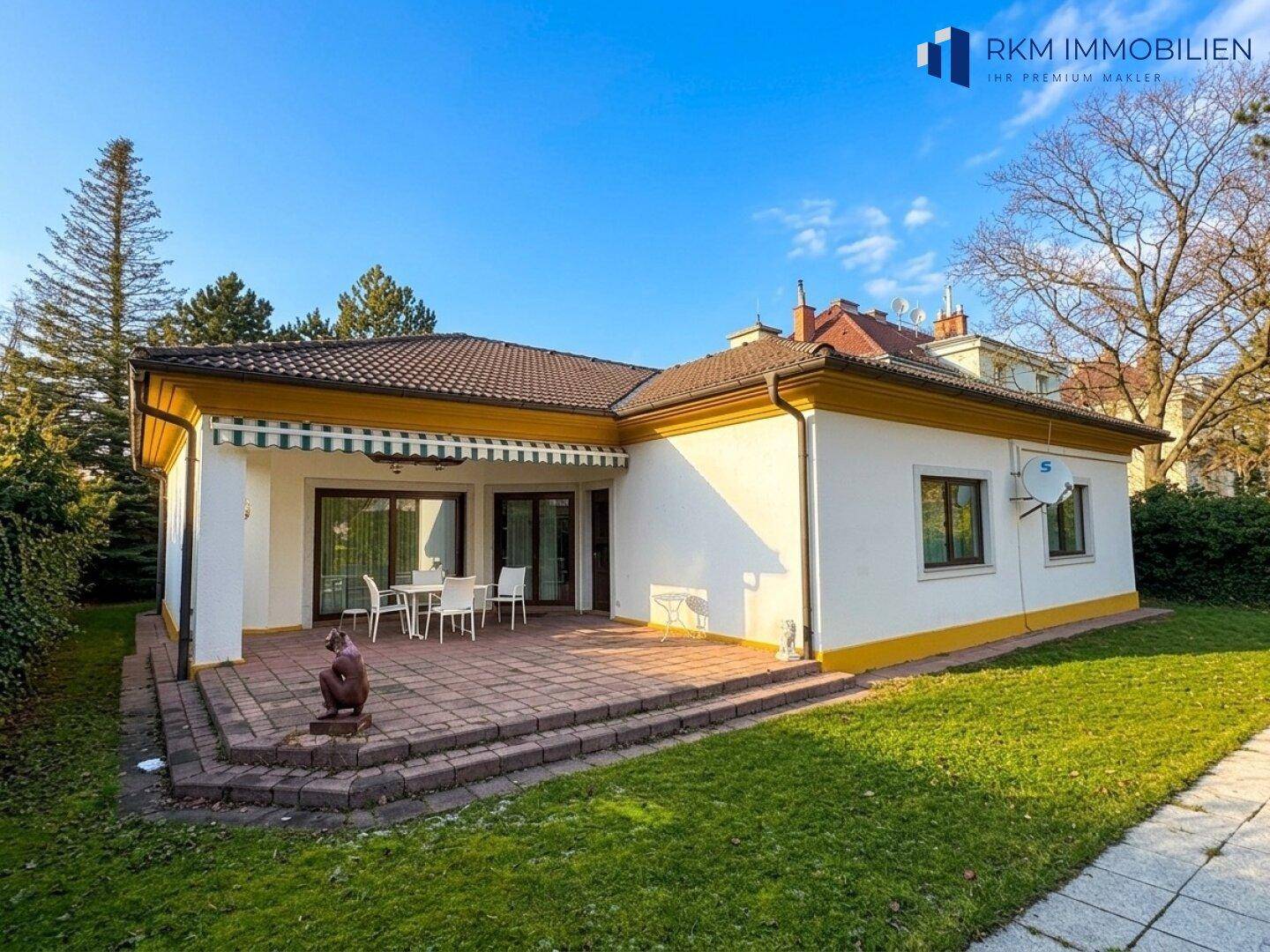 Hinteransicht des Hauses mit großer gepflasterter Terrasse, Gartenmöbeln und Markise.