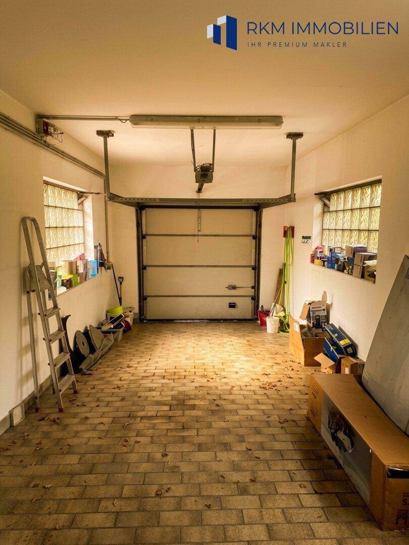 Geräumige Garage mit Rolltor, robustem Boden und praktischen Glasbausteinfenstern.