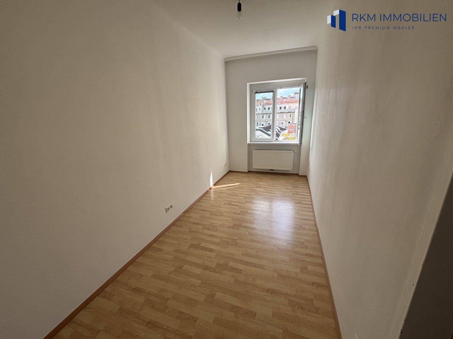 Schmaler Raum mit Parkettboden und einem Fenster, das einen Blick nach draußen bietet.