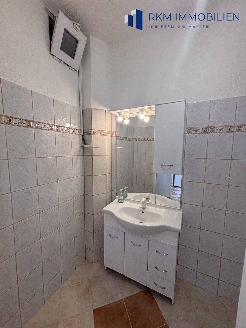 Badezimmer mit Waschbecken, Spiegelschrank und hellen Fliesen an den Wänden.