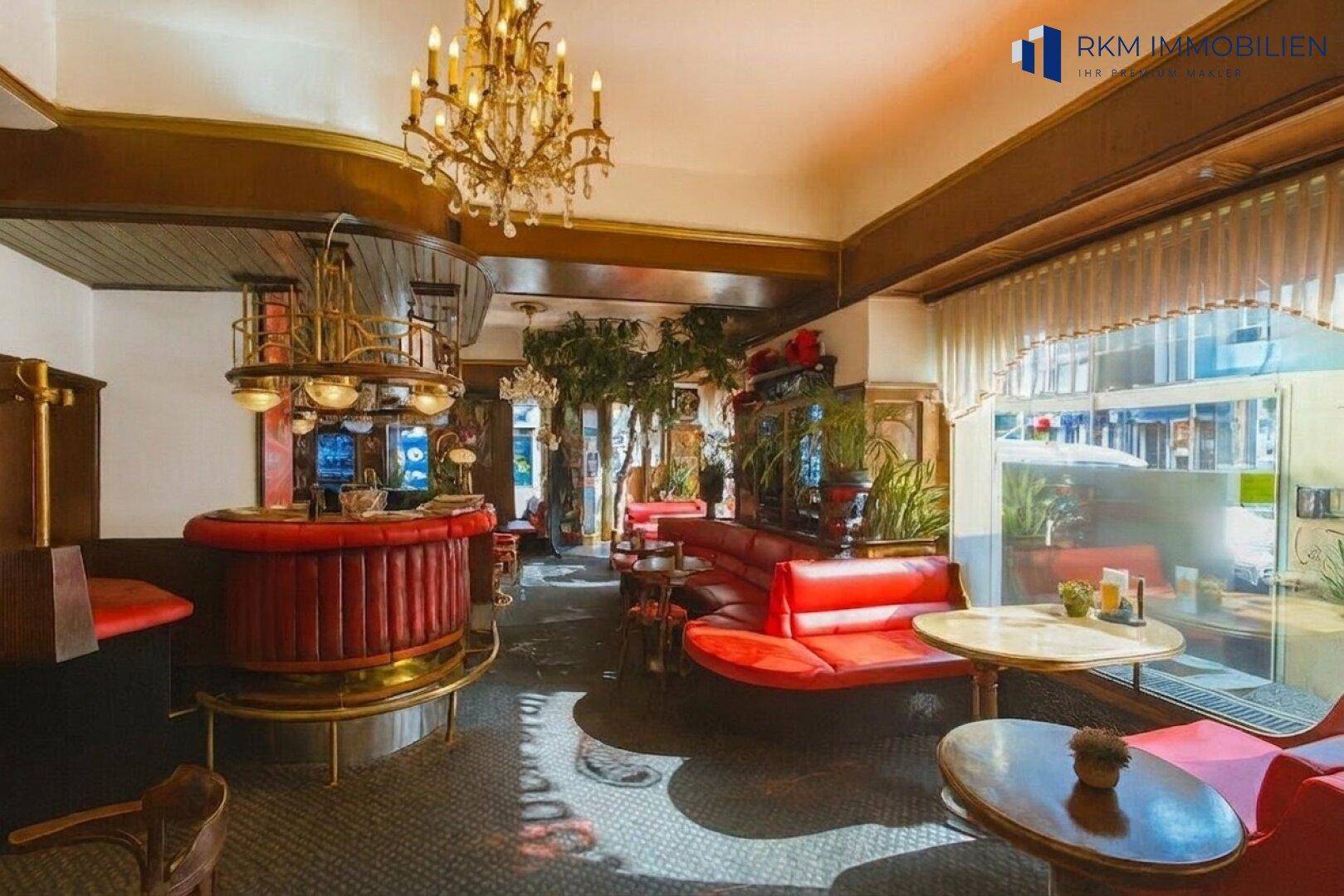 Gemütlicher Innenbereich einer Bar mit rotem Ledergestühl, dunklem Boden und einem opulenten Kronleuchter.